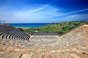 Ancient theater of Kourion with a semicircular seating area and a view of the Mediterranean coast.