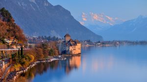 Chillon Castle on the lakeshore with calm water and high mountains in the background.