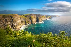 Cliffs of Moher with a long rocky coastline, green cliff tops and the sea along the steep rock faces.