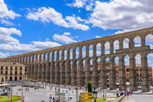Two tiers of arches of the Aqueduct of Segovia above a busy city square.