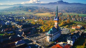 Fröhlicher Friedhof von Săpânța mit Kirche, Dorf und Hügellandschaft aus der Luft
