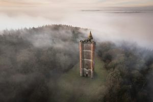 Aerial view of King Alfred’s Tower in a forest clearing, surrounded by dense mist