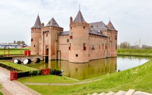 Muiderslot with brick towers, bridge, moat and green areas surrounding the castle.