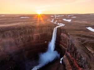 Aerial view of Hengifoss with the low sun, patches of snow and several waterfalls across the plateau.