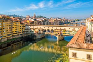 Ponte Vecchio with colourful bridge houses, several stone arches and rowing boats on the river.