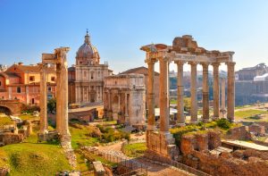 Roman Forum with tall columns, a stone arch, ruins and a dome in the background.
