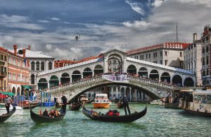 Rialto Bridge with several gondolas and boats on the busy canal in the foreground.