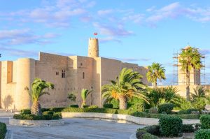 Ribat von Monastir mit hohen Festungsmauern, mehreren Türmen und Palmen im Vordergrund.