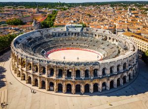 Aerial view of the Amphitheatre of Nîmes with its oval arena, seating, arcaded façade and surrounding city buildings.