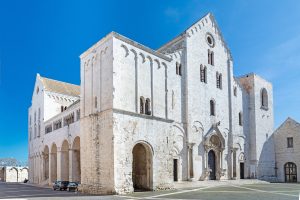 Schrägansicht der Basilika San Nicola in Bari mit heller Steinfassade, Arkaden und Vorplatz.
