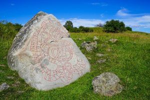 Large runestone at Birka and Hovgården with red-highlighted carvings in a green meadow landscape.