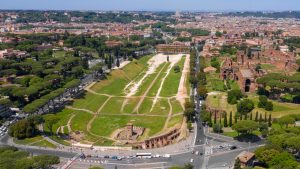 Aerial view of the Circus Maximus with a long green area, paths, rows of trees and adjacent ruins