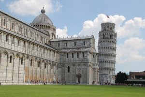 Leaning Tower of Pisa next to a large church building with a lawn in the foreground.